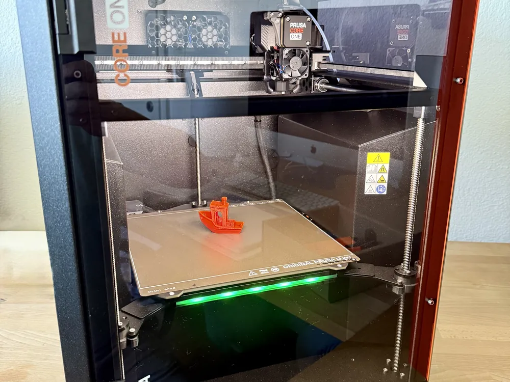 Prusa CORE One+ 3D-Drucker mit laufendem Druck und beleuchtetem Druckbett